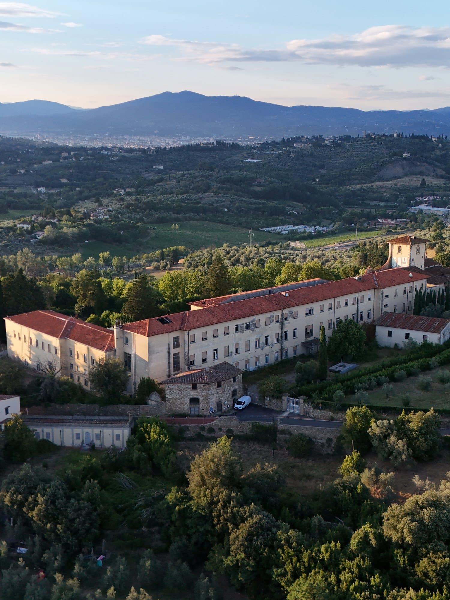 Un grande complesso storico sulle colline di Firenze al tramonto, con la città sullo sfondo